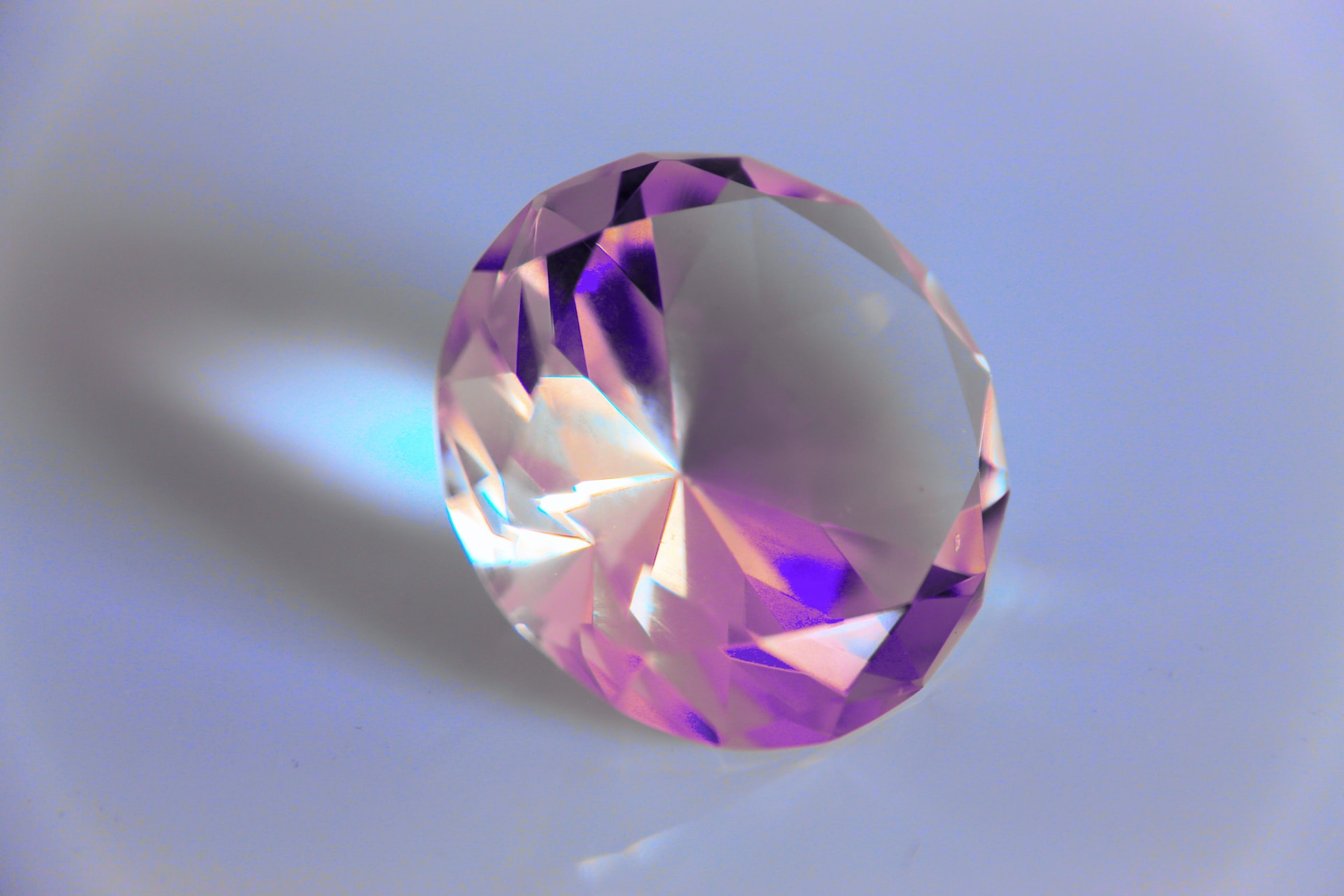 a pinkish-purple jewel sits on a light blue surface.